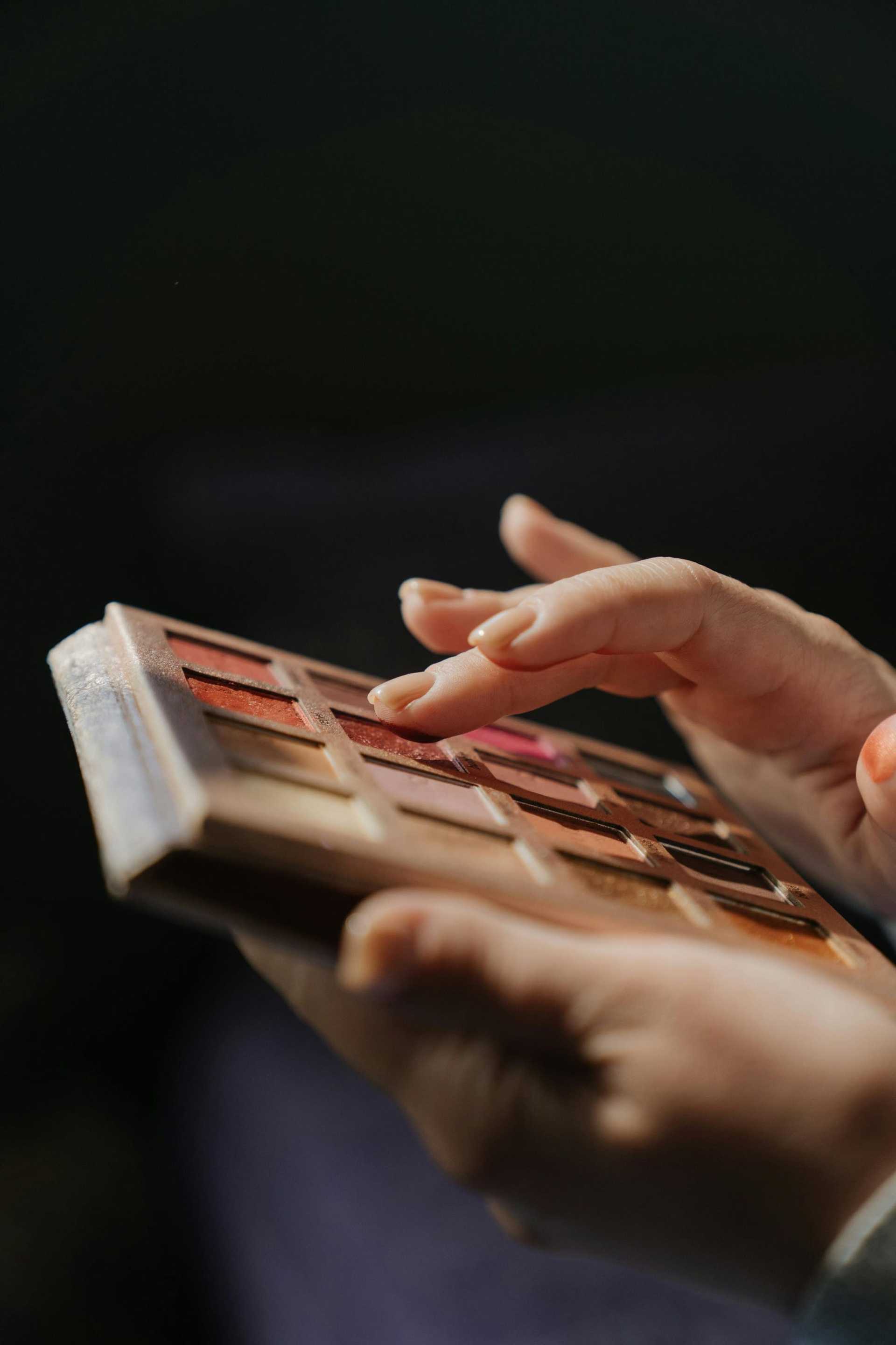 Hands applying makeup using a colorful eyeshadow palette.