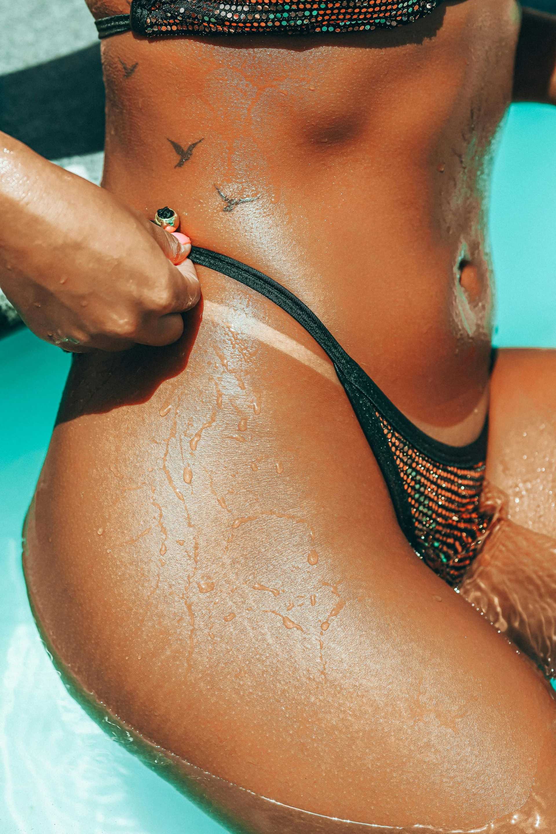 Person in swimwear adjusting bikini bottom while standing in a pool, with water droplets on skin.