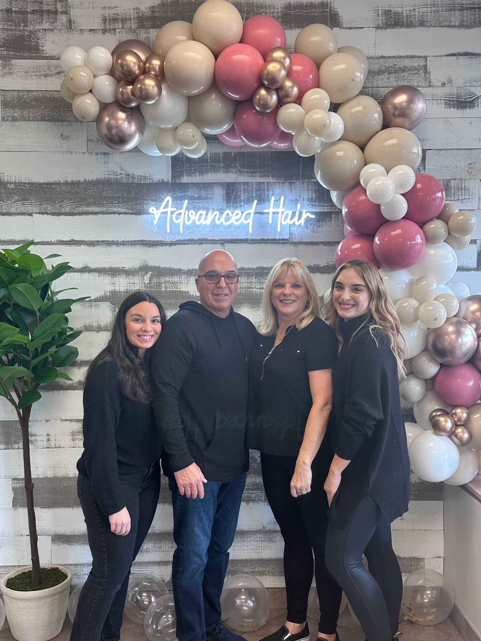 Group of four people standing under a balloon arch with the sign "Advanced Hair" in the background.